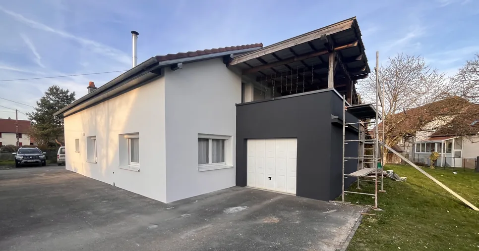 Maison du Sundgau après isolation extérieure, crépi blanc sur la façade et crépi anthracite sur le garage, échafaudage encore posé