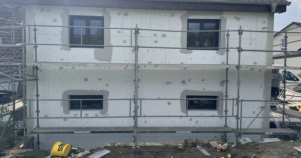 Pose d'une isolation extérieure Sto sur une maison du Sundgau, panneaux isolants chevillés et ébrasements de fenêtres enduits, échafaudage en place